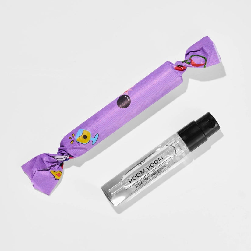 A small clear spray bottle with a black cap labeled 'ROOM SCENTS' lies next to a purple wrapped item with cartoon graphics, photographed on a light gray background.