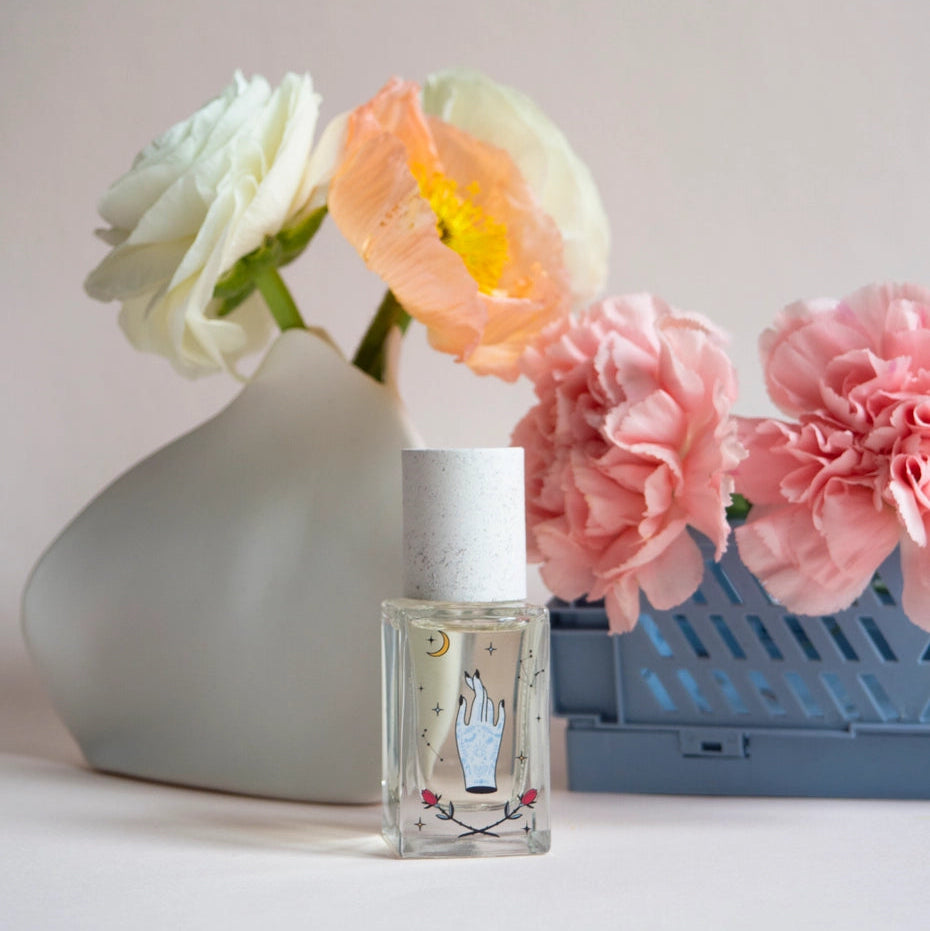 Small bottle with a design on a surface with flowers and a vase in the background