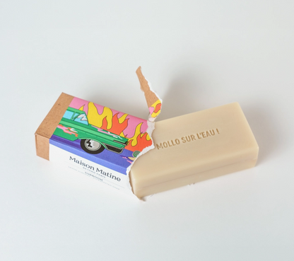 A beige bar of Maison Matine soap labeled 'MOLLO SUR L'EAU !' shown next to its colorful illustrated cardboard box on a clean white background.